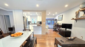 A modern kitchen with white cabinets, a central island, and a dining area with a white table and benches. - Peaceful 3 Bedroom 2 Bathroom Pool Home (Hollywood)