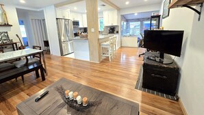 A spacious living area with a wooden floor, a dining table, a TV, and a kitchen in the background. - Peaceful 3 Bedroom 2 Bathroom Pool Home (Hollywood)