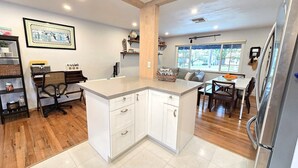 A modern kitchen with a central island, wooden flooring, and a dining area with a view of the outdoors. - Peaceful 3 Bedroom 2 Bathroom Pool Home (Hollywood)