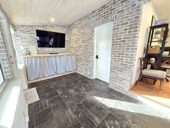 Una habitación con pared de ladrillo, un televisor de pantalla plana montado sobre un banco de madera y una puerta blanca.