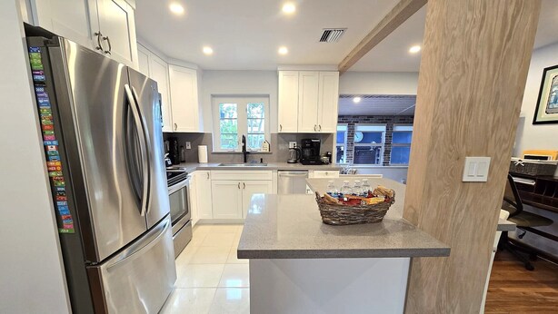 A modern kitchen with white cabinets, stainless steel appliances, and a central island with a basket of bottled water. - Peaceful 3 Bedroom 2 Bathroom Pool Home (Hollywood)