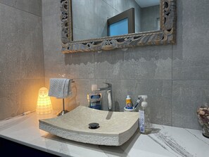 Ein Badezimmer mit einem Steinsink, einem Spiegel mit aufwendiger Holzarbeit, einem Handtuch und Toilettenartikeln.