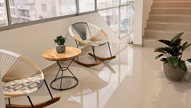Ein modernes Interieur mit Balkon, Korbschaukelstühlen, einem kleinen Holztisch mit Pflanze und einer Treppe, die zu einer oberen Etage führt.