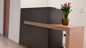 Ein dunkler Empfangstresen mit heller Holzauskleidung, ein Blumentopf mit Blumen sowie zwei Pendelleuchten.