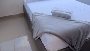 Ein modernes Schlafzimmer mit großem Fenster, einem ordentlich bezogenen Bett und Blick auf die Stadt.