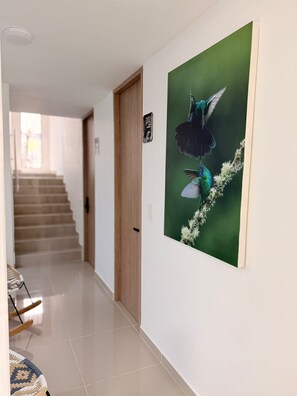 Un couloir avec un escalier, une porte en bois et un tableau représentant un colibri, accroché au mur.