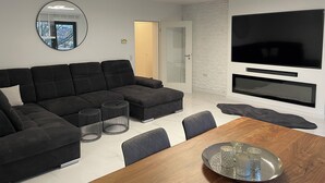 Ein modernes Wohnzimmer mit einer Eckcouch, einem Holzesstisch und einem flachbildfernseher an der Wand.