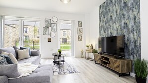 A modern living room with a grey sofa, a flat-screen TV, and a large abstract painting on the wall. - Stunning 3 Bedroom Home in Balsall Heath With Patio and Central Heating (Birmingham)