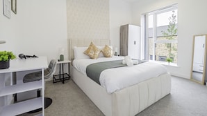 A modern bedroom with a large bed, a desk, and a window with a view of the outside. - Stunning 3 Bedroom Home in Balsall Heath With Patio and Central Heating (Birmingham)