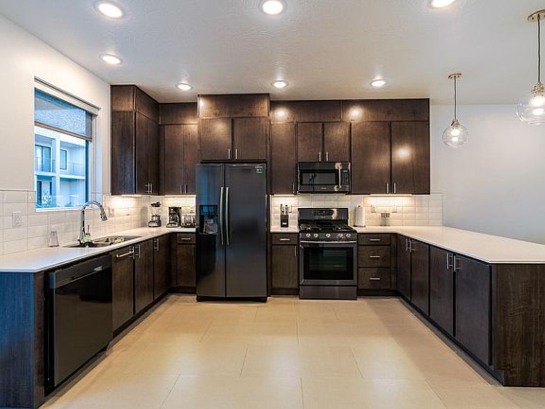 Una cocina moderna con armarios de madera oscura, electrodomésticos de acero inoxidable y un amplio ventanal que proporciona luz natural.