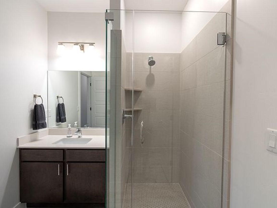 A modern bathroom with a glass-enclosed shower, a large mirror, and dark-toned cabinets.