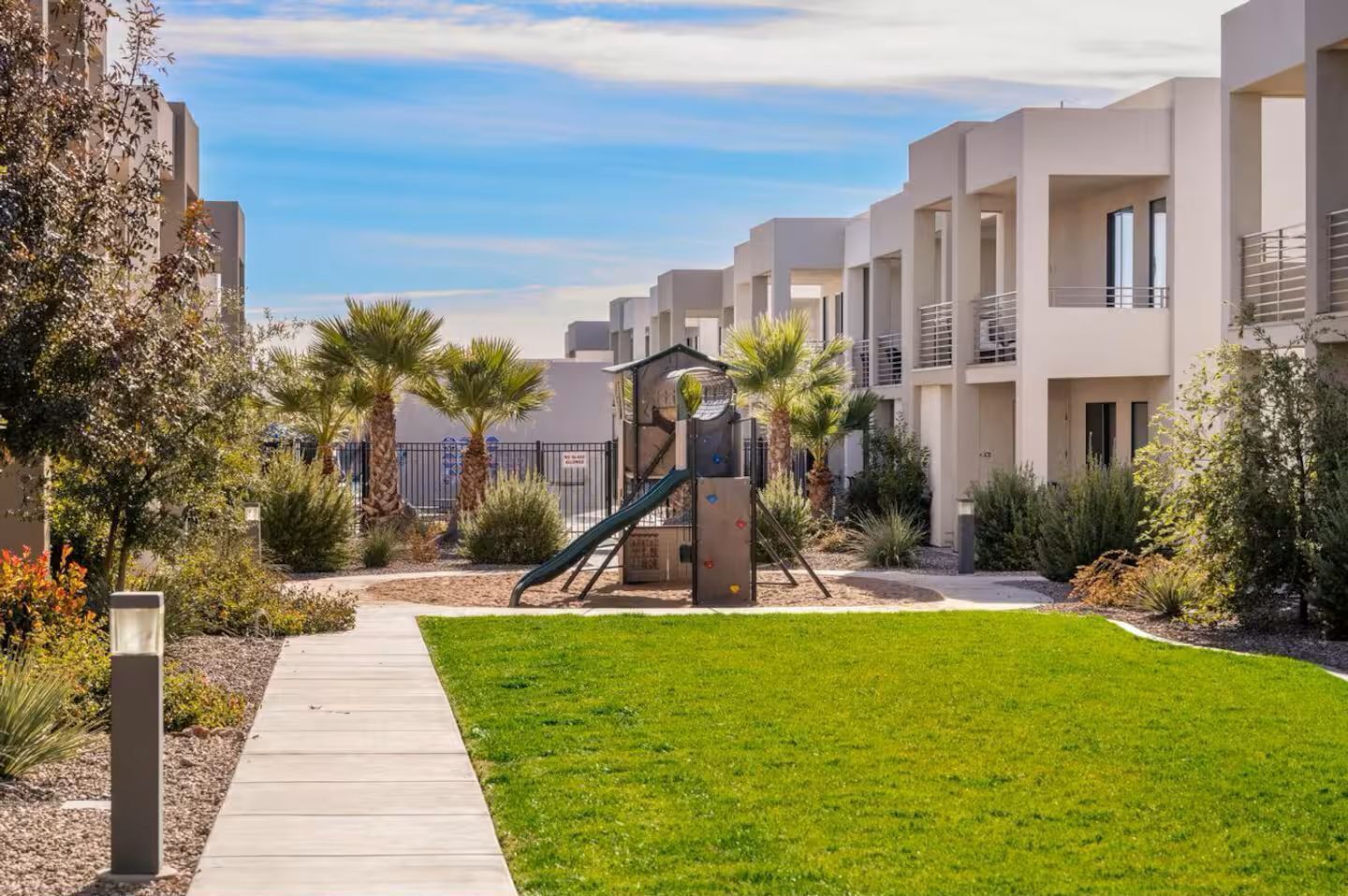Un edificio residencial con un parque infantil, un espacio con césped y un sendero.