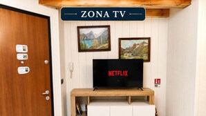 Une pièce avec un téléviseur posé sur un meuble en bois, sur lequel est apposé le logo « NETFLIX », une enseigne « ZONA TV » au-dessus, et deux tableaux encadrés accrochés au mur.