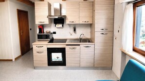 A compact kitchen with a dishwasher, microwave, and a window with curtains.