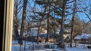 A wooden deck with a metal table and blue chairs, surrounded by snow-covered ground and trees. - Entire House. 2+ bed, 2 bath near Lake & bikeway (Burlington)