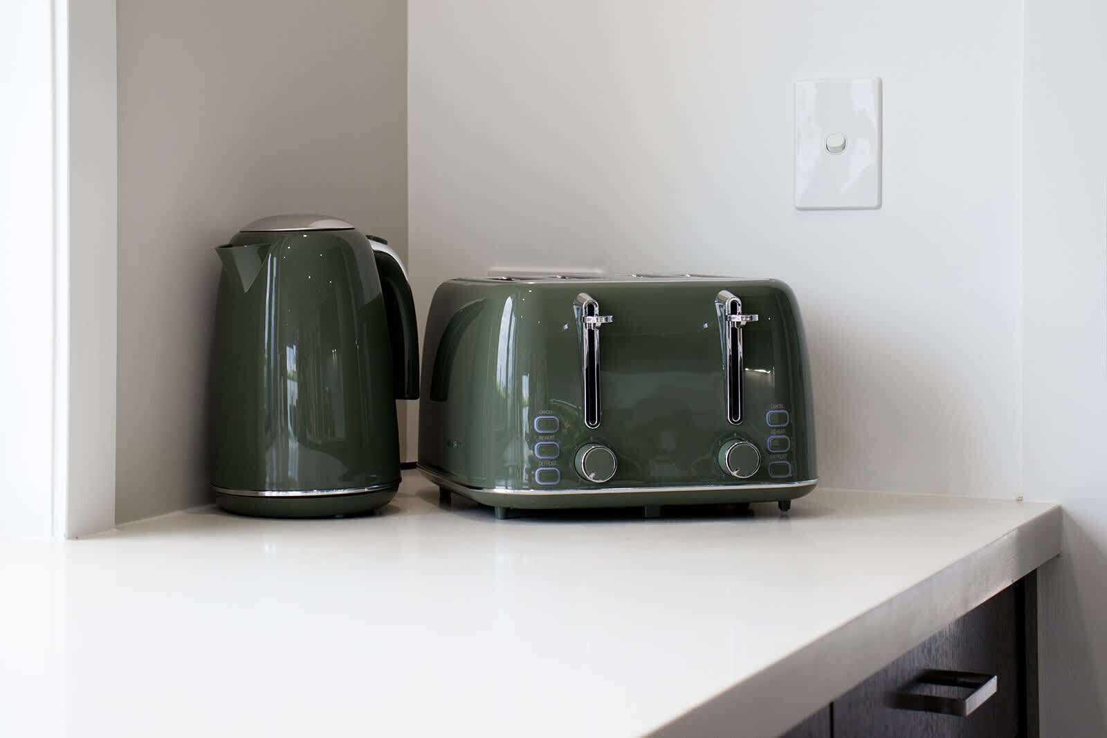Zwei grüne Geräte, ein Wasserkocher und ein Toaster, stehen auf einer weißen Arbeitsplatte.