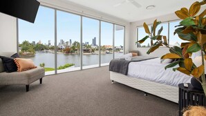 Ein modernes Schlafzimmer mit einem großen Bett, einer Couch und Blick auf eine Stadtlandschaft und Wasser.