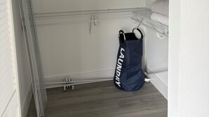 Un lavadero con estanterías metálicas, una lavadora y una bolsa azul con la etiqueta "LAUNDRY".