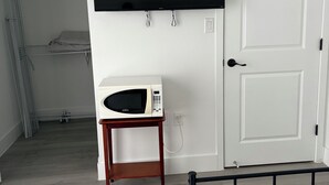 Una habitación con cama, un microondas sobre una mesita, un armario y una puerta.