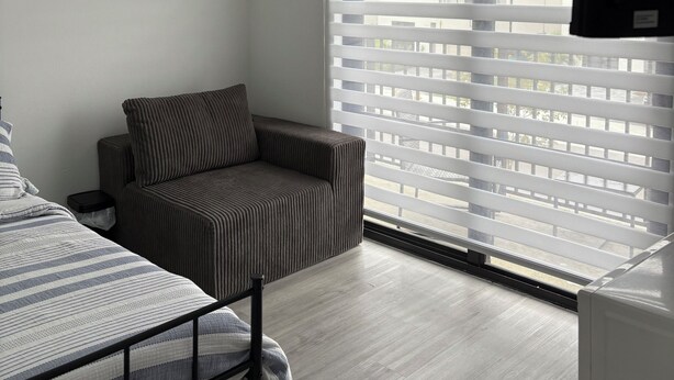Una habitación con cama, sofá, televisor y ventana con persianas.