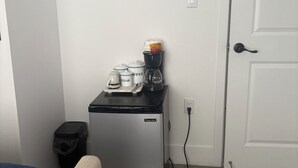 Eine kompakte Küchenzeile mit kleinem Kühlschrank, einer Kaffeemaschine und einem Mülleimer.