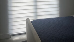 Ein Schlafzimmer mit einem Bett, einem Fenster mit Jalousien und einem Teppichboden.