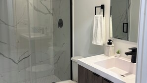 Ein modernes Badezimmer mit einer Duschkabine, einer weißen Toilette und einem Waschtisch mit Spiegel.
