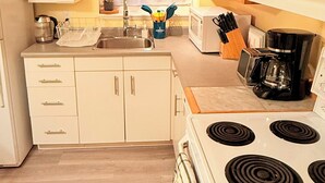 A compact kitchen with white cabinets, a stove, a microwave, and a sink. - Cozy 3 bedroom suite in heart Kitsilano, close to kits beach & downtown (Vancouver)