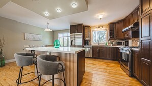 A modern kitchen with wooden cabinets, stainless steel appliances, and a central island with bar stools. - Spacious, Newly Renovated, Centrally Located | TMH (Burlington)