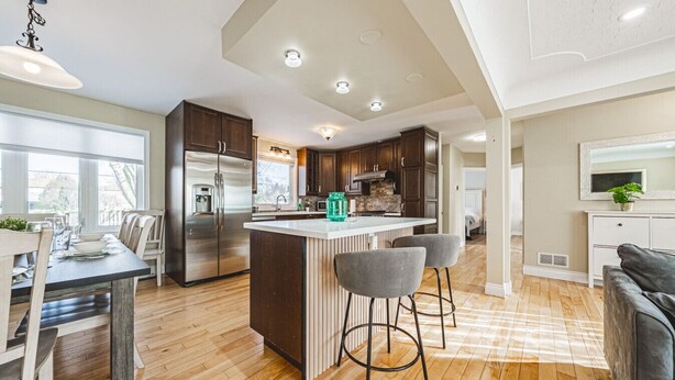 A modern kitchen with a central island, bar stools, and a dining area with a table and chairs. - Spacious, Newly Renovated, Centrally Located | TMH (Burlington)
