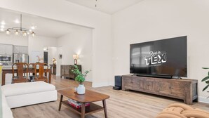 En moderne stue med et fladskærms-tv, møbler i træ og et spiseområde i baggrunden.