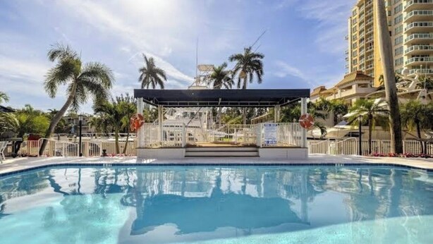 Une piscine dotée d’une zone abritée, de palmiers et, au loin, d’un immeuble de grande hauteur.