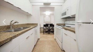 Une cuisine compacte avec des meubles blancs, des plans de travail en granit, un four à micro-ondes encastré et un coin repas comprenant une table et des chaises.