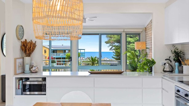 A modern kitchen with a large window offering a view of the sea and buildings.