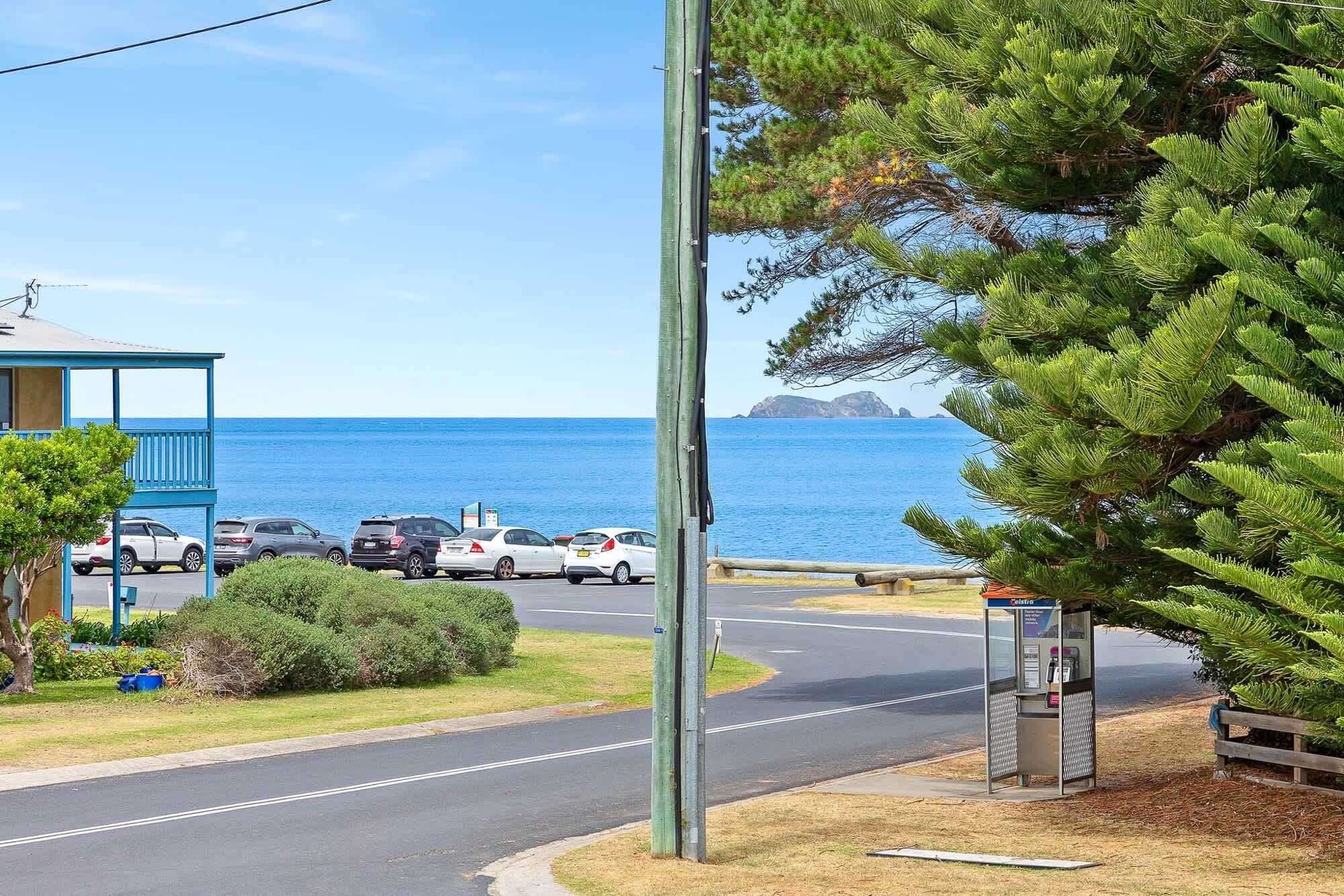 A coastal road with parked cars, a blue building, and a telephone booth.