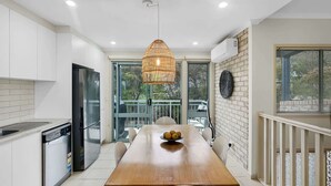 A modern kitchen with white cabinets, a wooden dining table, and a hanging light fixture.
