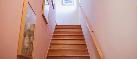 Una scala in legno con corrimano che conduce a un pianerottolo con un quadro incorniciato.