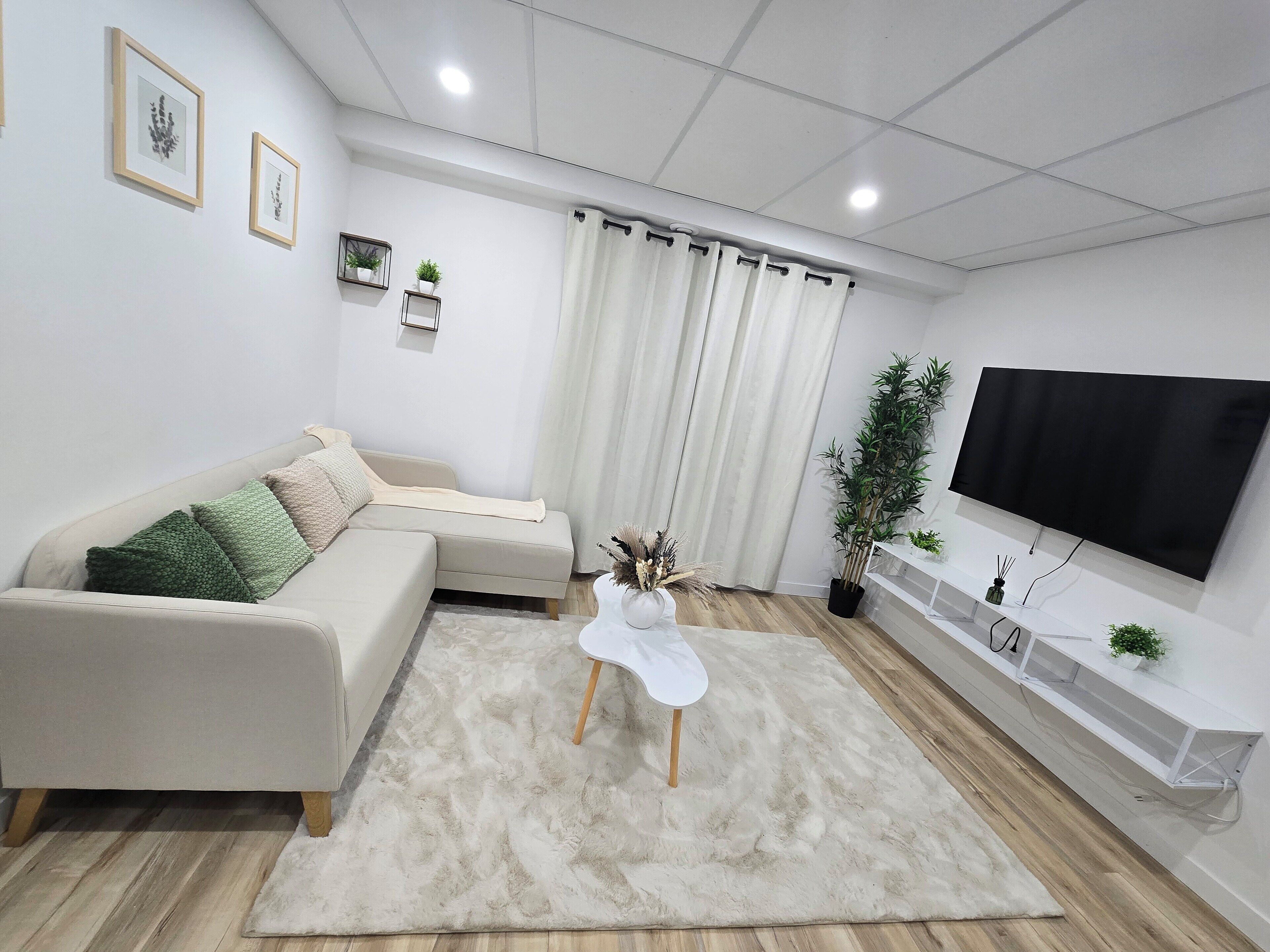 A modern living room with a sectional sofa, a flat-screen TV, a white coffee table, and a potted plant.