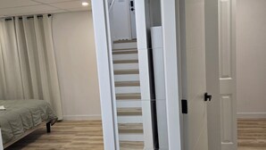 Una habitación moderna y bien iluminada, con suelo de madera, una cama con colcha verde y una escalera que conduce a otra habitación.