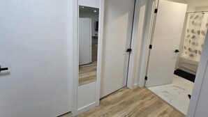 Un pasillo con puertas blancas, suelo de madera y zona de ducha con cortinas estampadas con motivos de hojas.