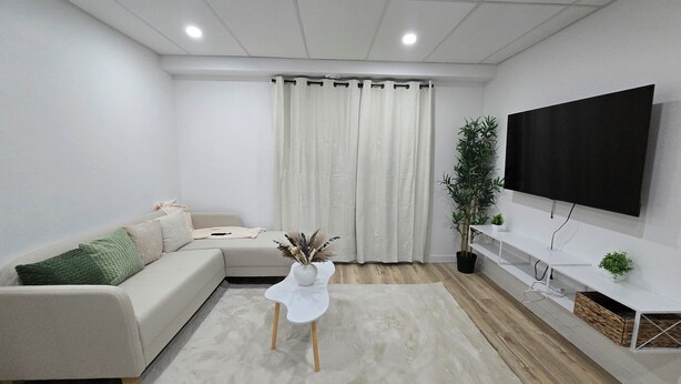 Ein modernes Wohnzimmer mit einem Ecksofa, einem weißen Couchtisch, einem flachbildfernseher an der Wand und einer Topfpflanze.