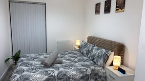 A bedroom with a bed, nightstands, a lamp, a clock, and a potted plant. - Luxury 2 bedroom, 2 Bathroom Balcony Apartment (London)
