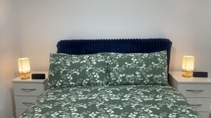 A bed with a floral bedspread, two bedside tables with lamps, and a dark blue headboard. - Luxury 2 bedroom, 2 Bathroom Balcony Apartment (London)