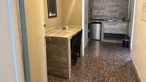 Een smalle gang met een kitchenette, inclusief een koelkast, spoelbak en betegelde spatwand.