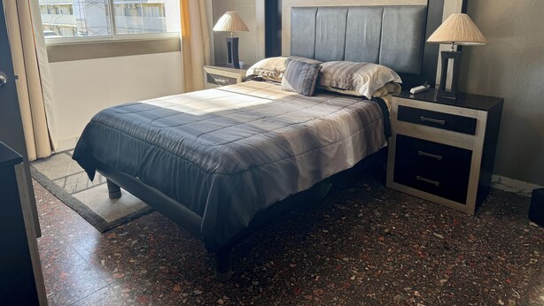 Een hotelkamer met een bed, twee nachtkastjes, een raam met gordijnen en uitzicht op gebouwen.
