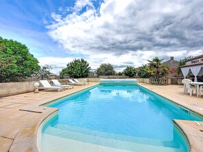 Una piscina rectangular con sillones de descanso y una mesa a la derecha.