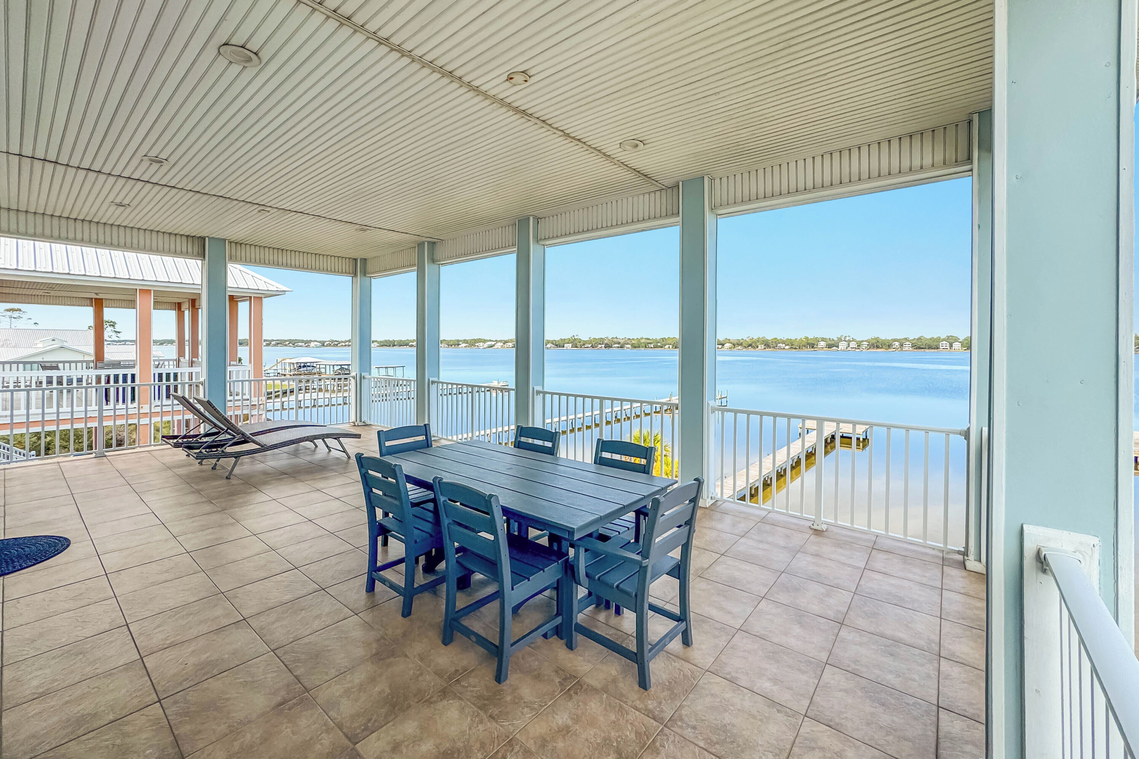 Ein überdachter Außenbereich mit Esstisch und Stühlen, einem Liegestuhl am Pool und Blick auf das Wasser.
