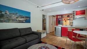 A modern living room with a grey sofa, a round coffee table with remotes, and a dining area with red chairs and a white table. - Family Time Duplex Family Getaway with Pool (Providencia)