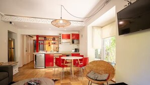 A modern kitchen with red cabinets, a dining area with red chairs, and a wicker chair with a cushion. - Family Time Duplex Family Getaway with Pool (Providencia)