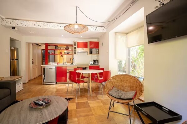 Une cuisine moderne avec des meubles rouges, un coin repas avec des chaises rouges et un fauteuil en osier avec un coussin.